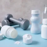 Dumbbells, creatine, water bottle and towel on a light blue surface.